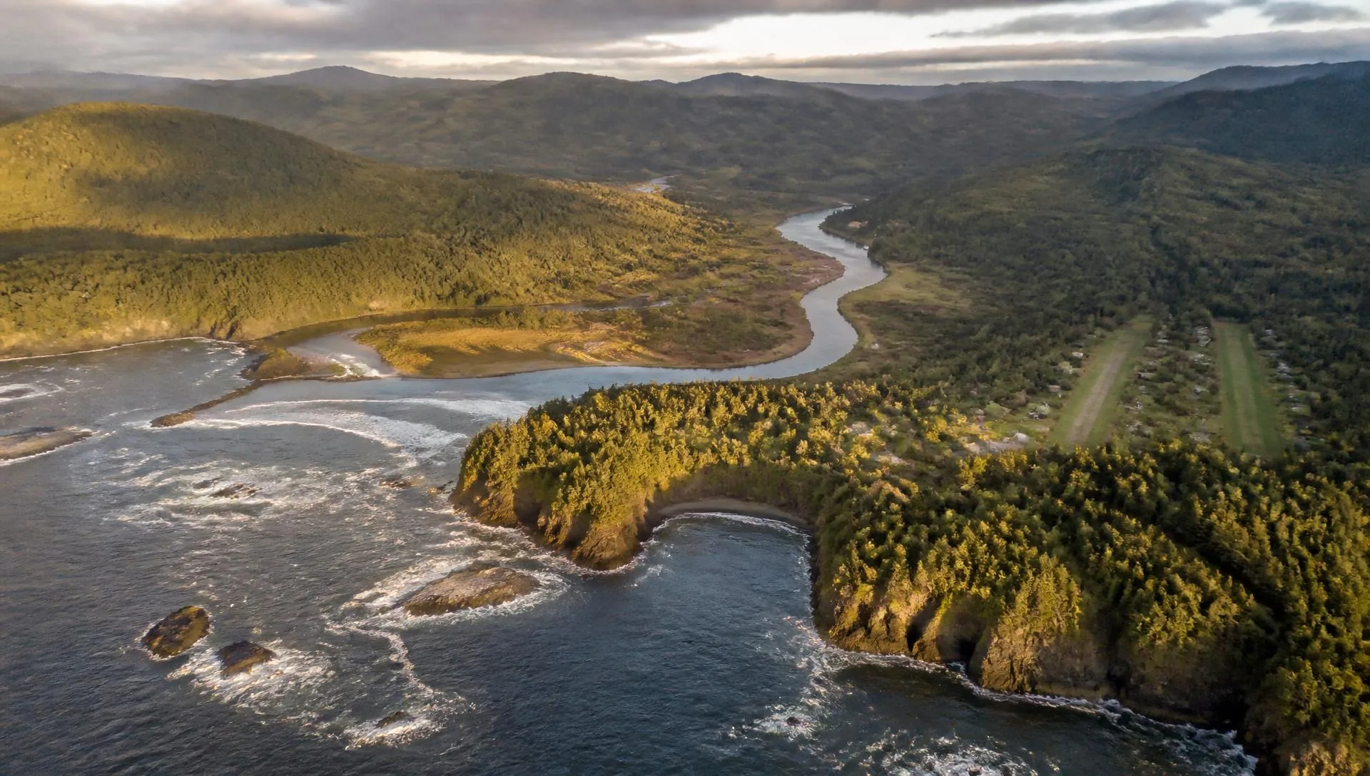Aerial view of the Oregon coast where a river valley, forest and a small remote community meet the Pacific.